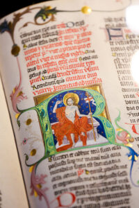 illuminated page of ancient bible with small religious painting and colorful text