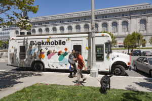 Photo of modern bookmobile in white with colorful caricatures of children and books on the side