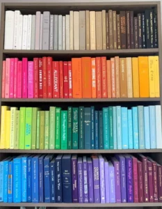 stacks of paperback books by color: red, orange, pink, green, blue, purple, brown